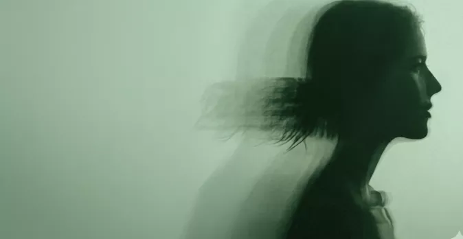 A blurred long-exposure silhouette of a woman's profile with flowing hair against a soft green background.
