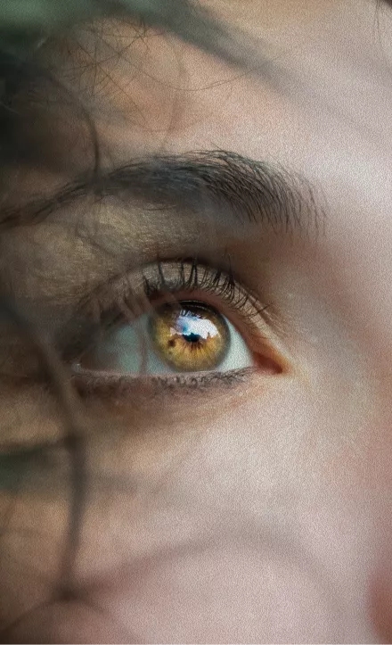 An extreme close-up of a person's hazel eye with dark lashes and visible skin texture in warm natural light.