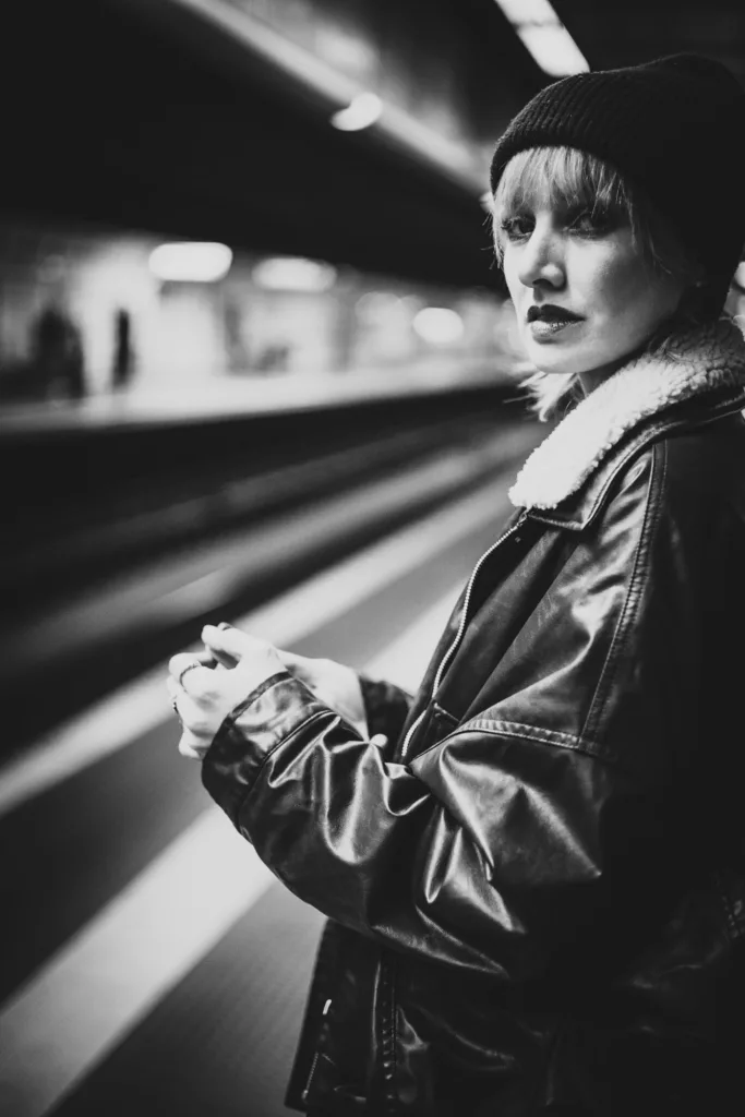 Frau mit Wollmütze und Lederjacke wartet auf einem U-Bahnsteig, Schwarz-Weiß-Porträt